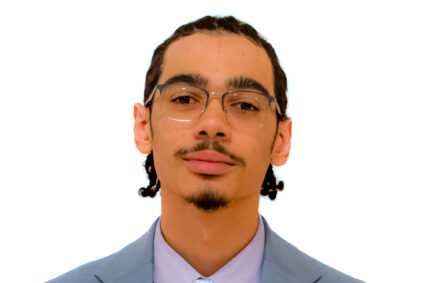 Professional headshot of Christian Houck, President of the Goucher College Student Government Association, in a blue suit and lavender shirt